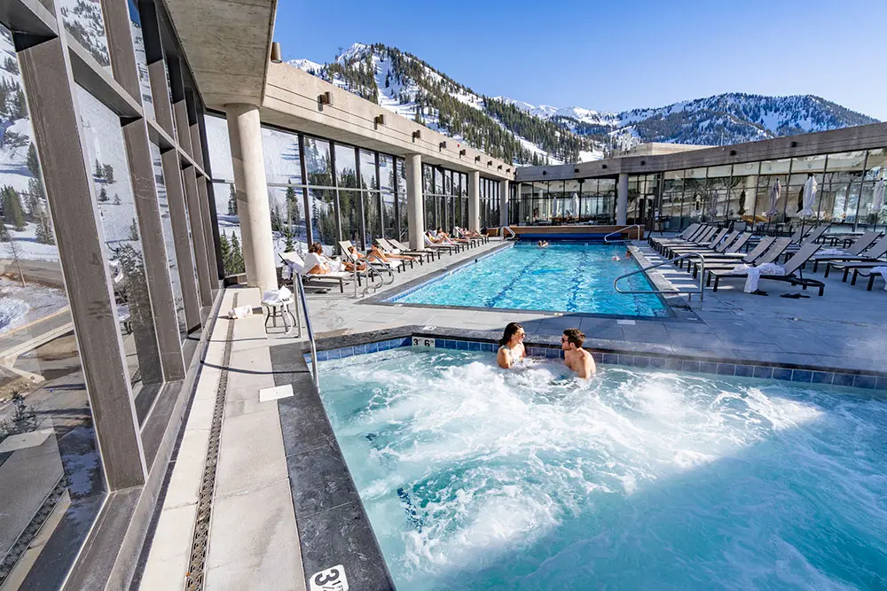 The rooftop pool and hot tub at Snowbird's cliff spa. A couple sits in the hot tub with a mountain view