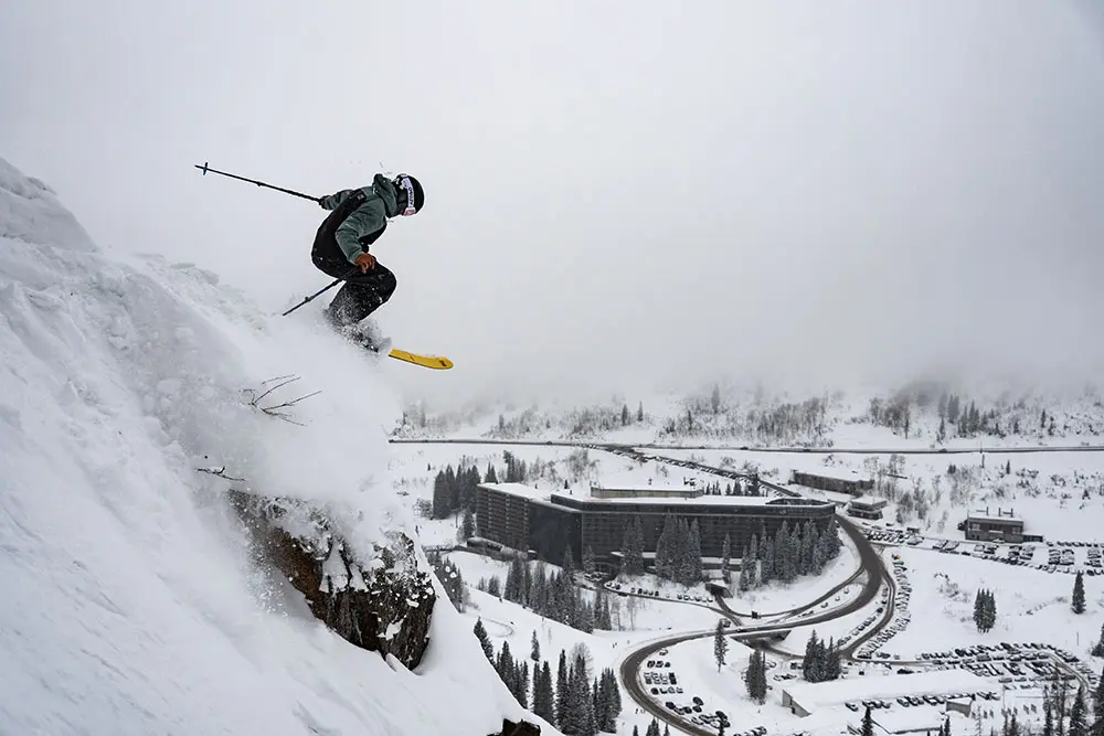 A skier jumps off a cliff with the cliff lodge in the background.